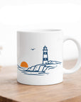 Weiße Keramiktasse von maavr mit minimalistischem Leuchtturm-Motiv an der Küste mit Sonne und Möwe – maritimes Nordsee Design auf Holztisch