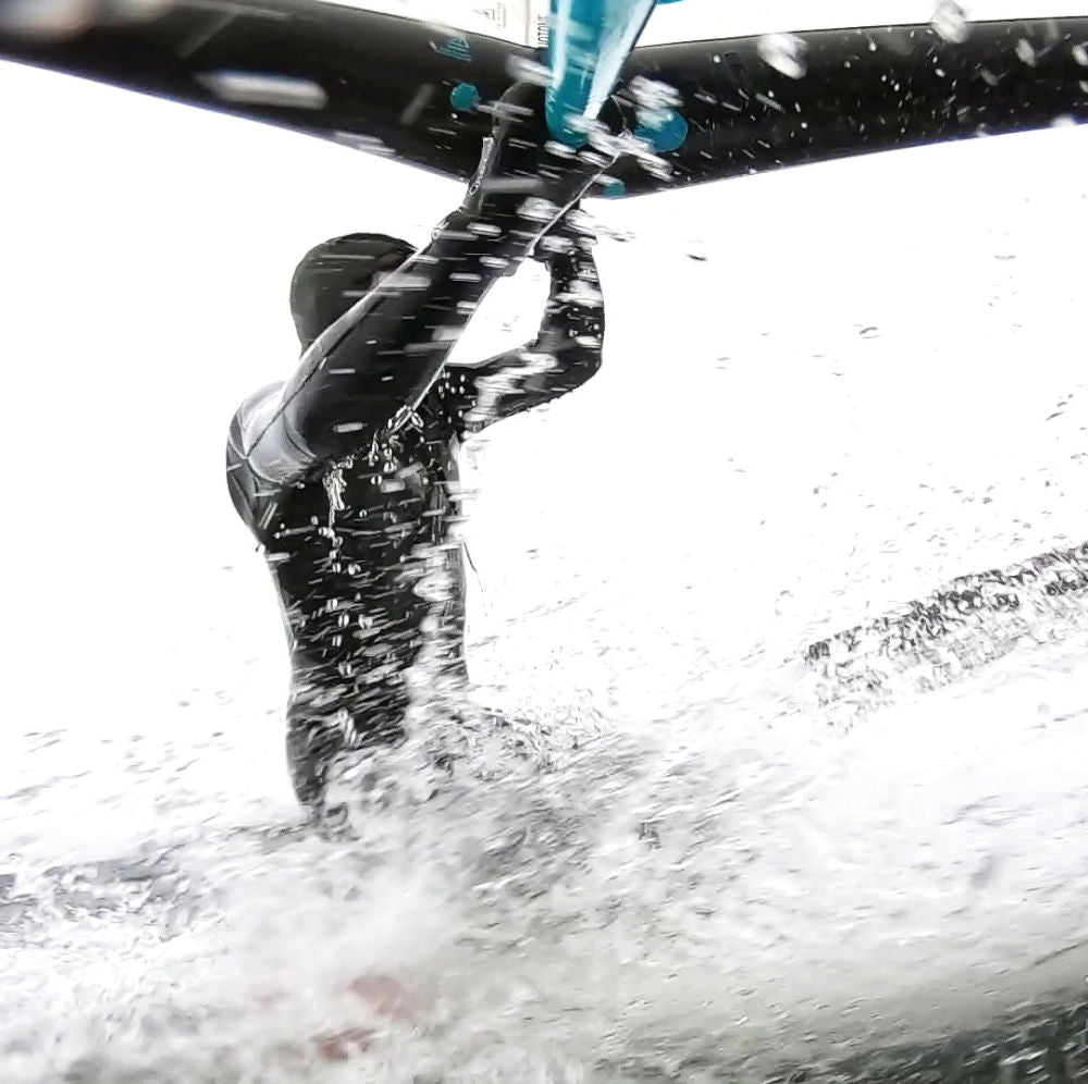 Wingfoiler landet kniend auf dem Board im Wasser