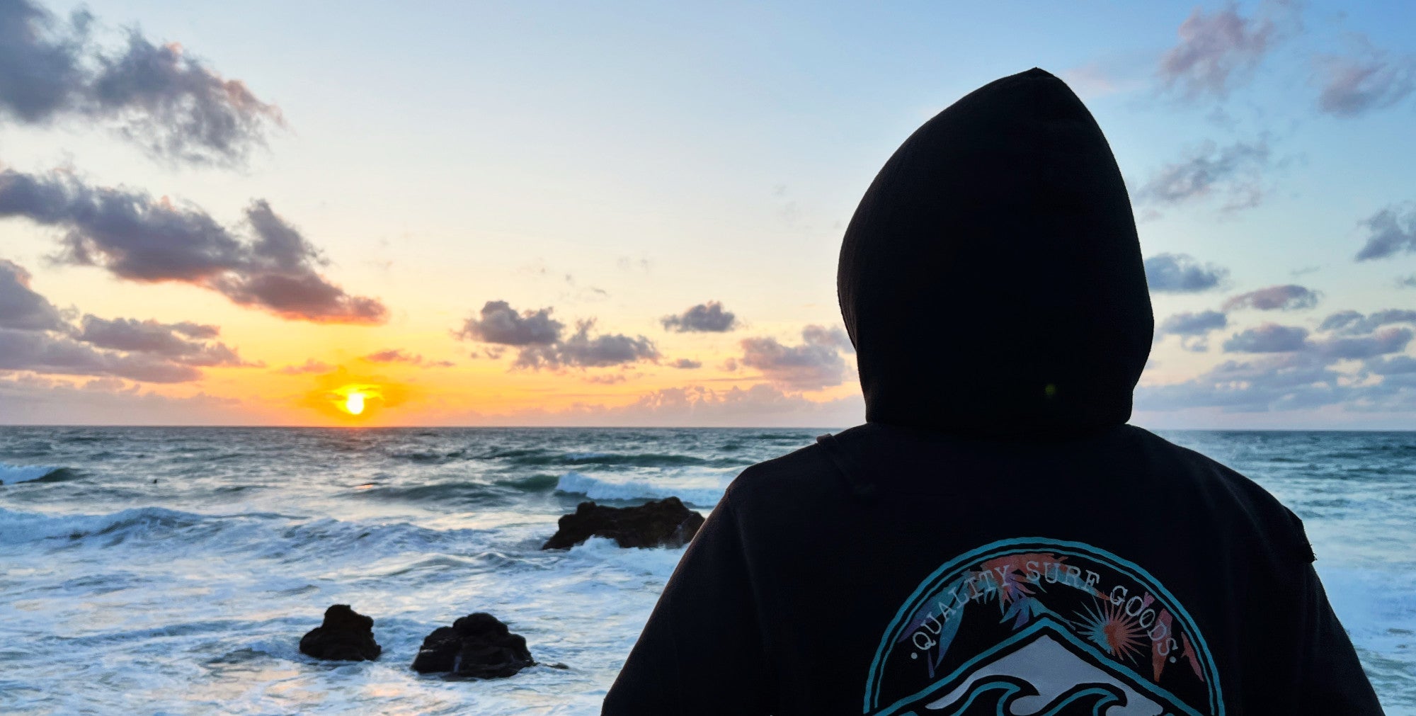 Shoulder Shot einer Person mit Hoodie, die den Sonnenuntergang am Meer betrachtet - Lifestylefoto für maavr