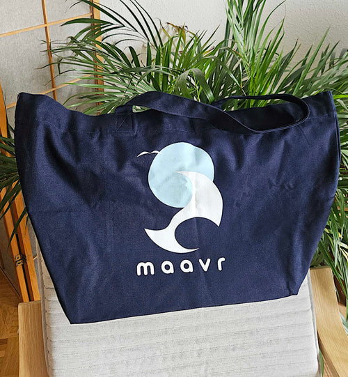 Große dnkelblaue Strandtasche aus Baumwolle mit maavr Logo auf Lounge-Stuhl vor einer Palme 