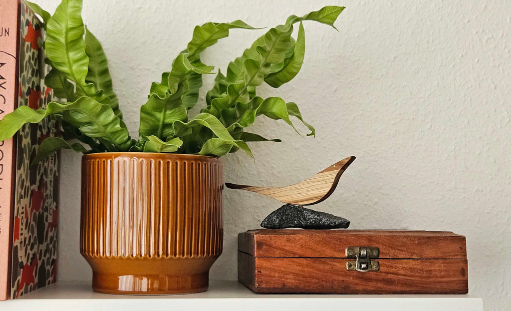 Holzvogel mit Intarsien auf Naturstein auf einer Holzbox neben einer Zimmerpflanze