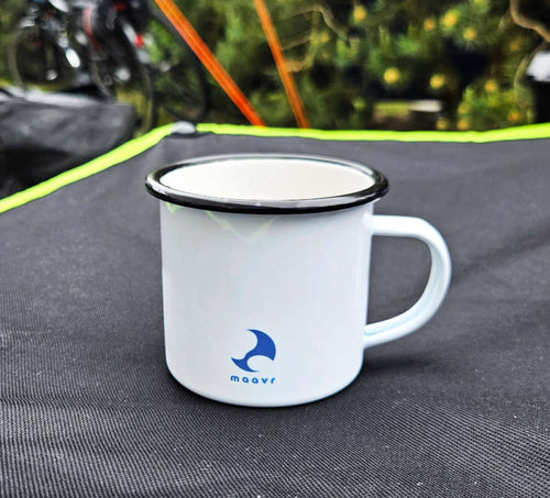 Weiße Emaille-Tasse mit schwarzem Rand und  blauem, kleinen maavr-Logo auf Campingtisch