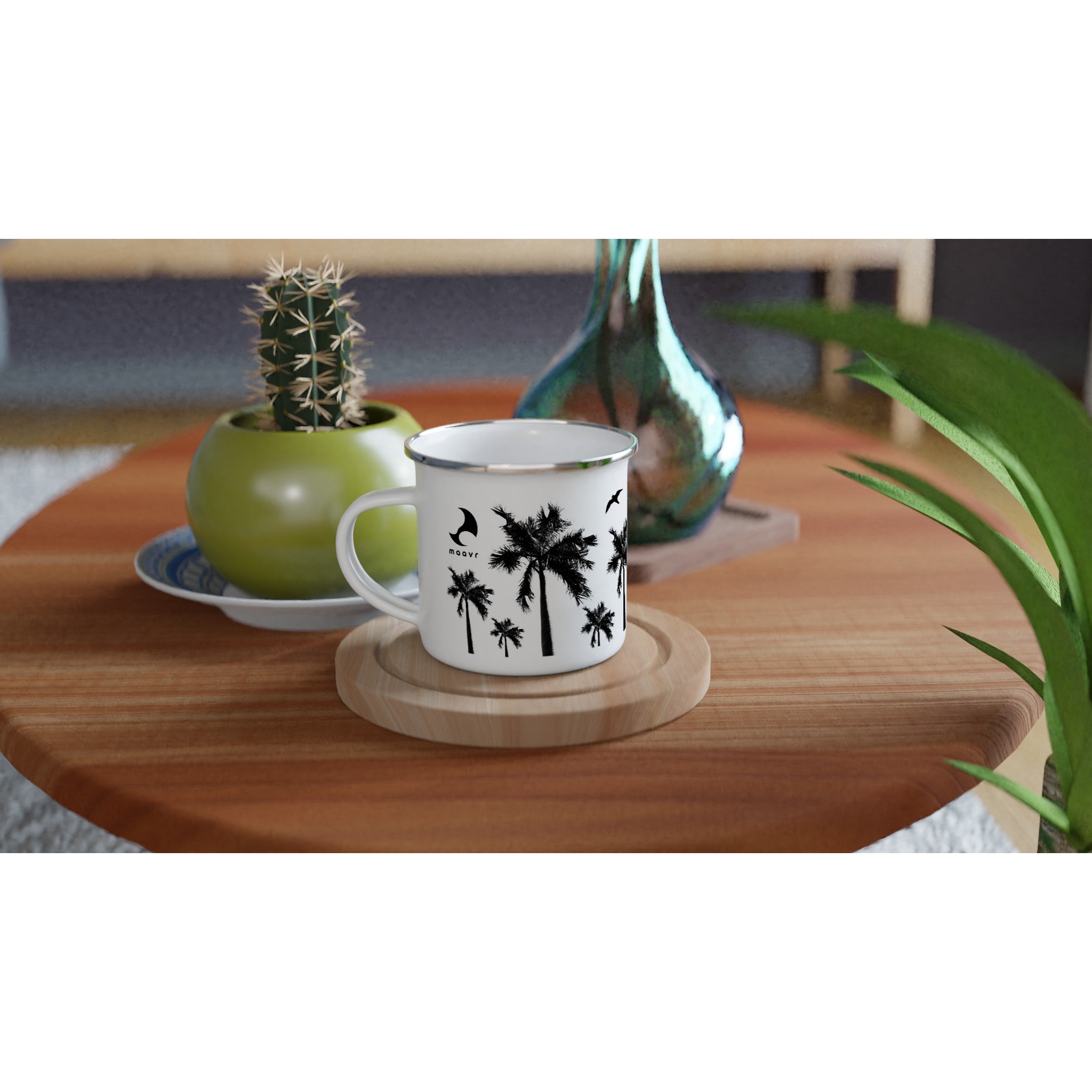 Weiße Emaille-Tasse mit silbernem Rand schwarzen Palmen-Motiven, maavr Logo auf Holztisch arrangiert mit Kaktus und Vase