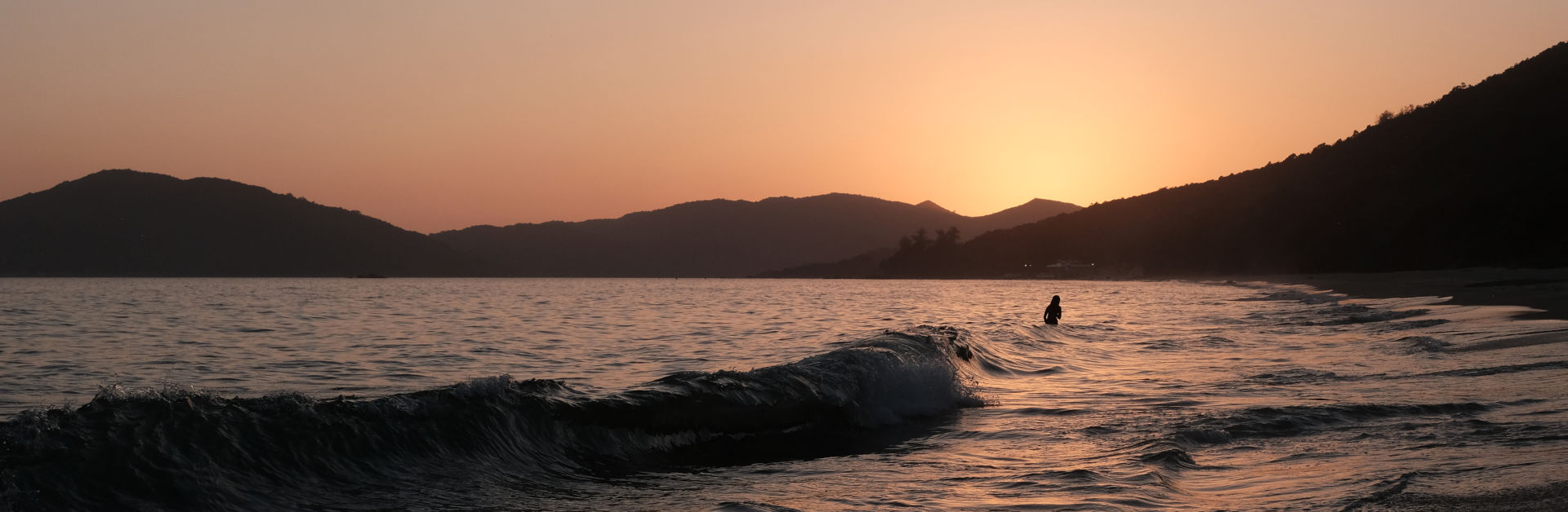 Person steht in der Abenddämmerung im Wasser am Strand