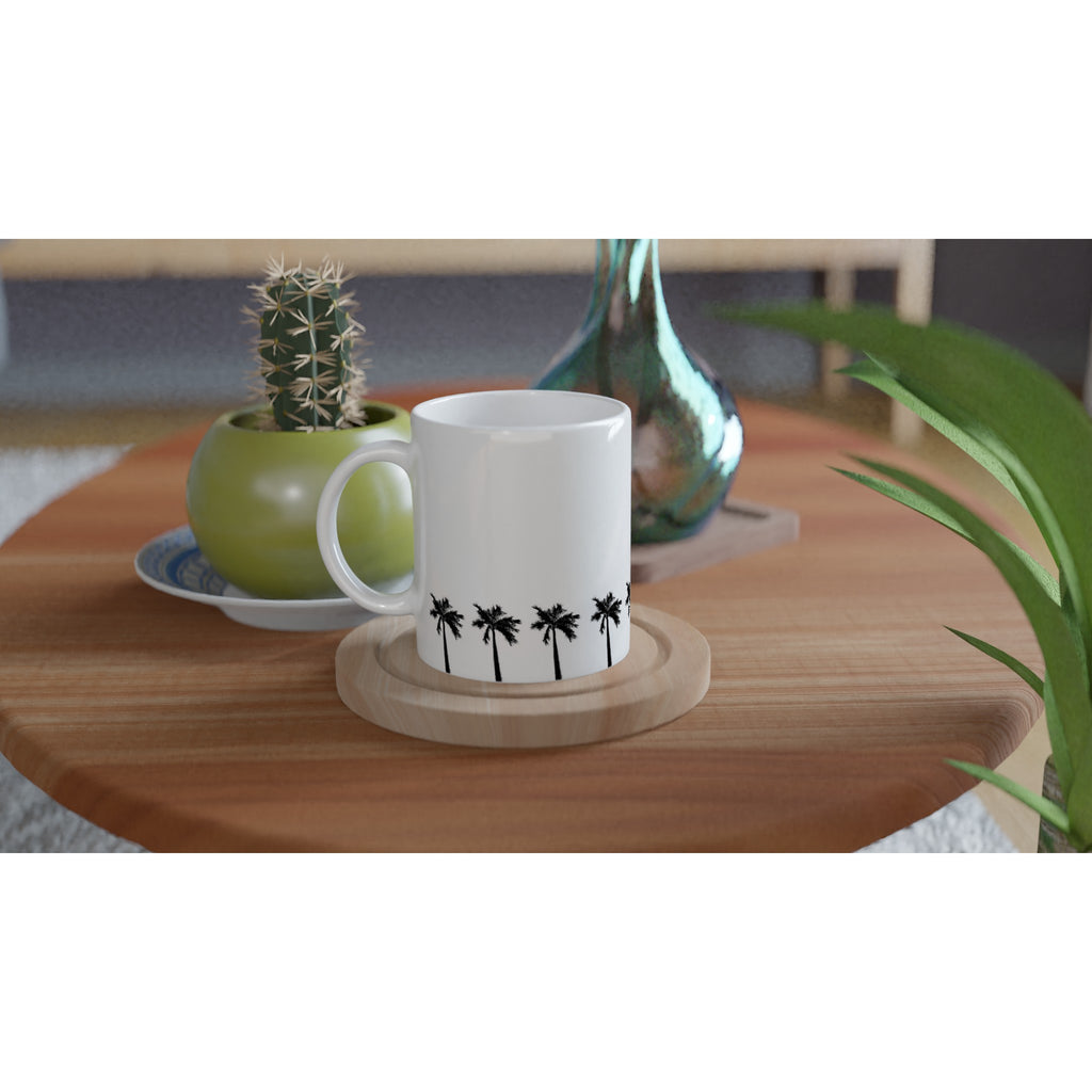 Weiße Keramiktasse mit umlaufender Palmenreihe auf Holztisch arrangiert mit Kaktus und Vase