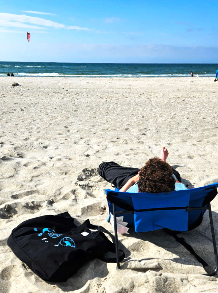 Person liegt auf Beach-Lounger am Strand und schaut Richtung mehr