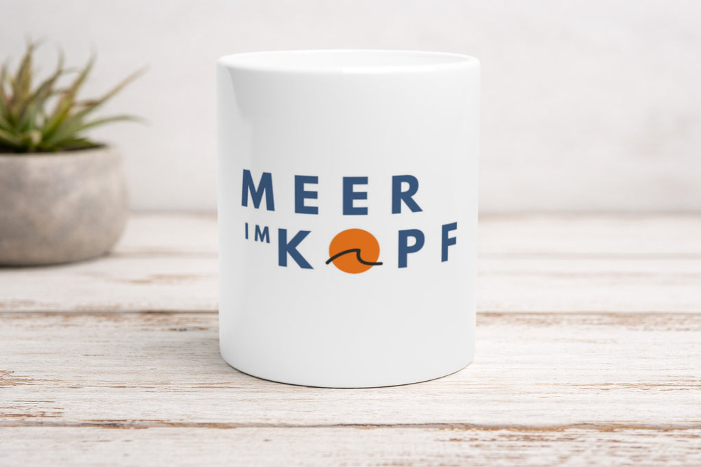 Weiße Keramiktasse mit maritimem Schriftzug „Meer im Kopf“ und Wellen-Symbol auf Holztisch – minimalistisches Küsten Design