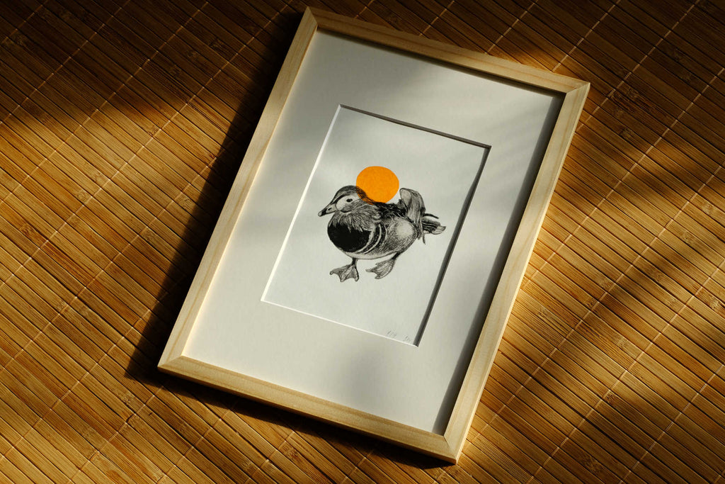 Gerahmte Original-Radierung Pato mit Entenmotiv und orangefarbener Sonne auf einer bambusmatte.
