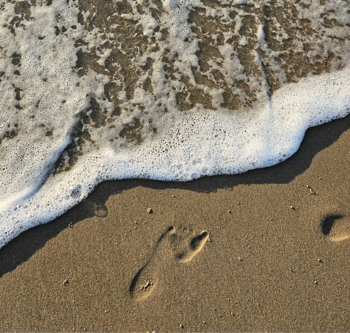Fußabdruck im Sand am Strand mit einlaufendem Wasser und warmem Lichteinfall
