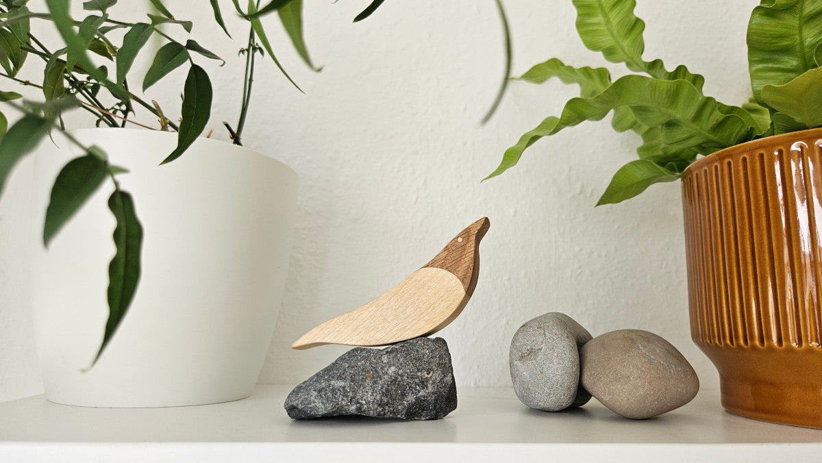 Möwe aus Holz auf dunklem Felsenstein, arrangiert auf weißem Regal neben Pflanzentöpfen