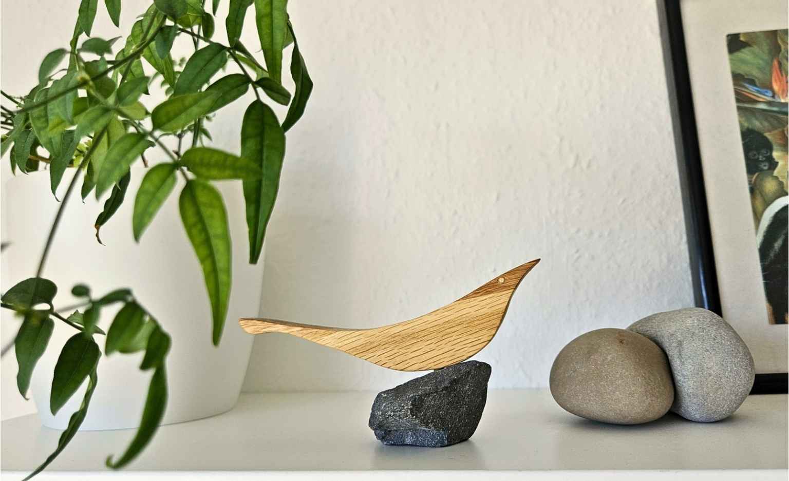 Handgefertigter Holzvogel auf Stein als maritime Deko auf einem Regal mit Pflanzen