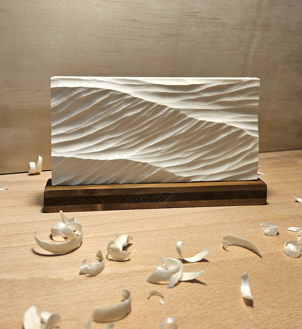 Swell Waves – handgeschnitztes Wellenrelief auf dunklem Holzsockel, auf einer Werkbank mit Holzspänen