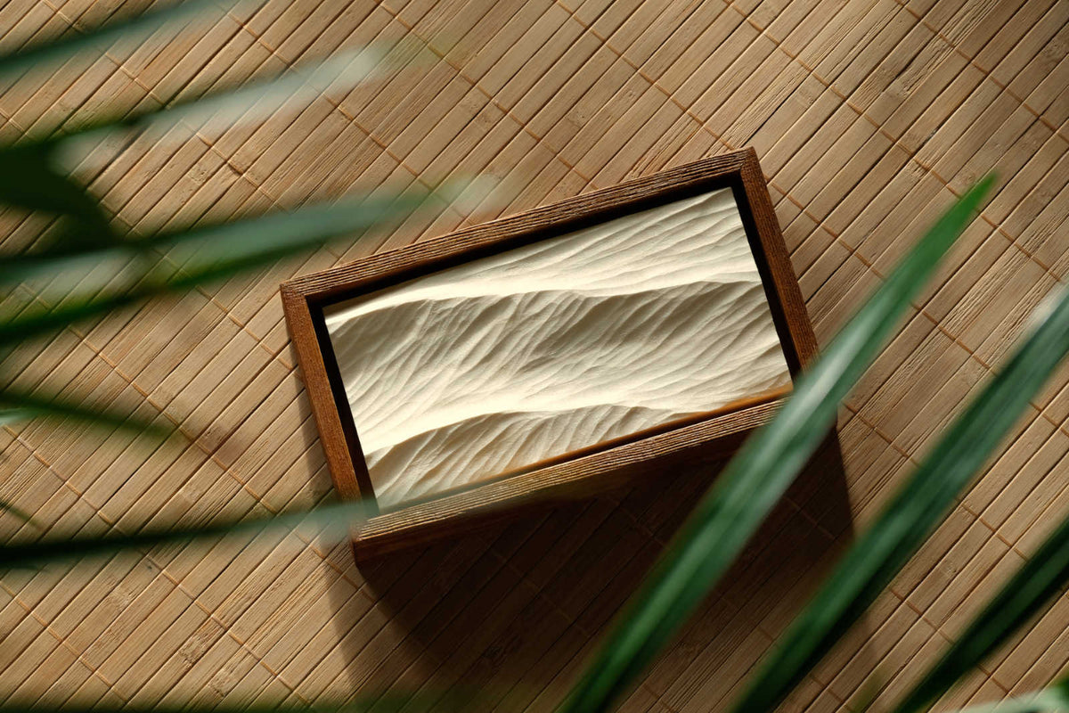 Gerahmtes Wellenrelief aus Holz auf einer Bambusmatte in einem Wohnraum zwischen Pflanzen