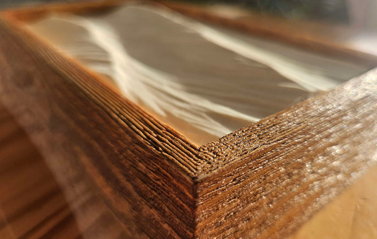 Nahaufnahme der Ecke des braunen Holzrahmens mit eingesetztem, handgeschnitztem Wellenrelief.