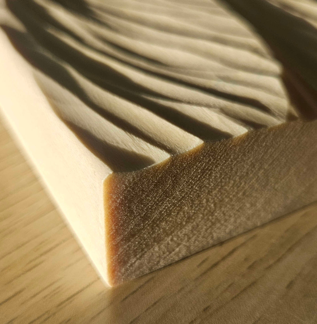 Nahaufnahme der handgeschnitzten, geschwungenen Wellenstrukturen im hellen Holz.