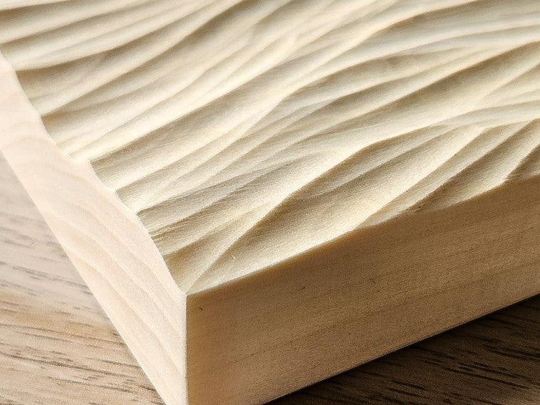 Detailaufnahme der von Hand geschnitzten Wellenstruktur im hellen Eschenholz